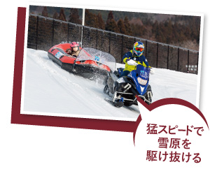 スノーモービルでラフティングボードを引っ張り、雪原を滑走している写真