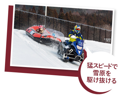 スノーモービルでラフティングボードを引っ張り、雪原を滑走している写真