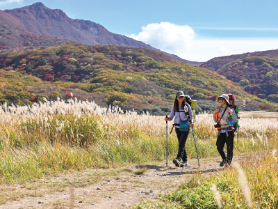 秋の山道をトレッキングする2人の女性